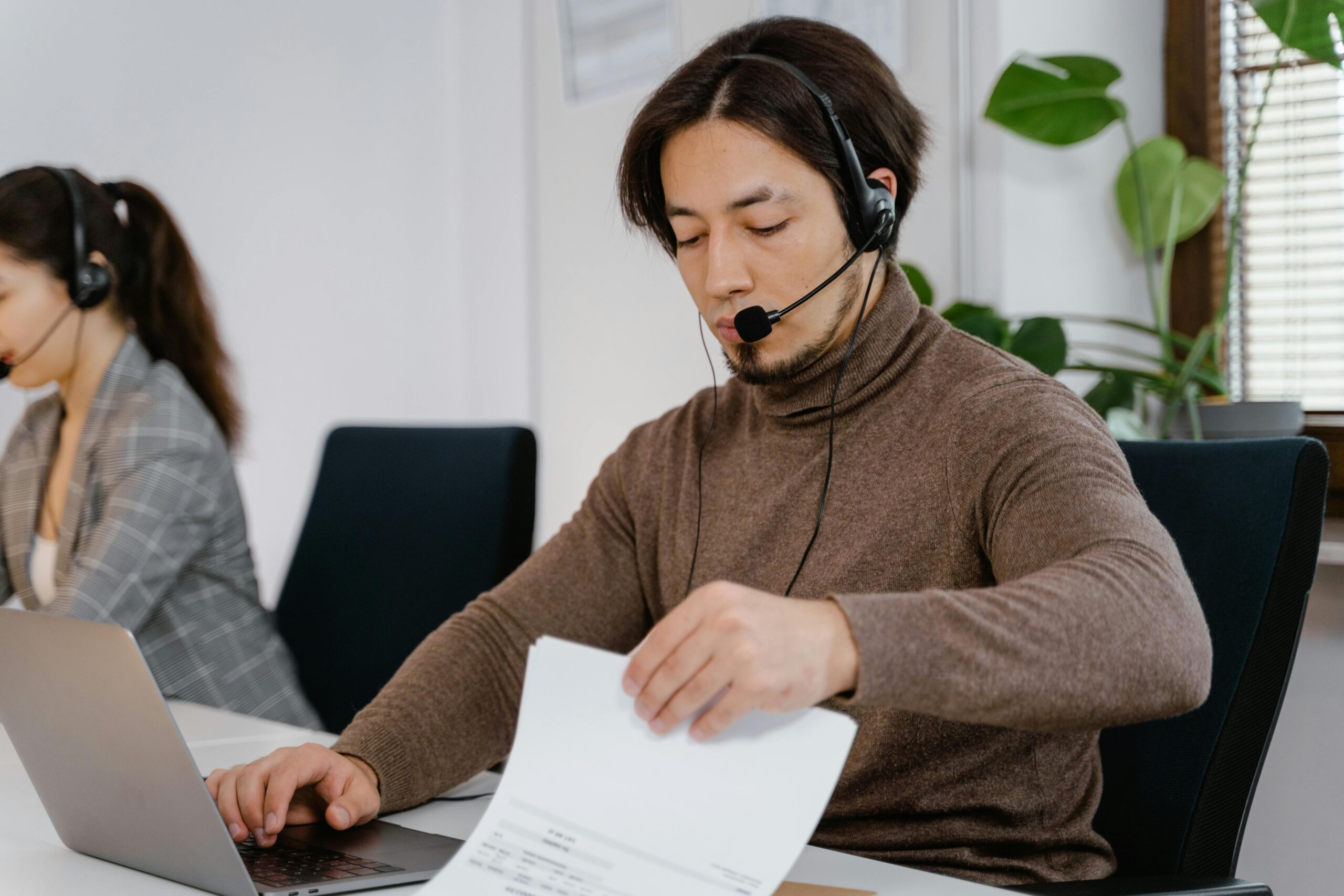 Man in headset working at a desk with laptop and papers in a modern office.